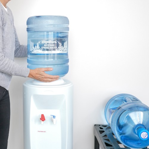 putting a 5 gallon water bottle on a white water cooler in office