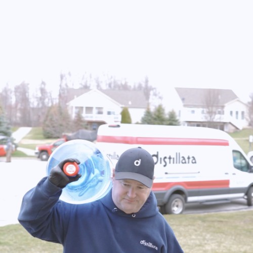 Distillata delivery driver carrying a 5-gallon water bottle to the front door of a house