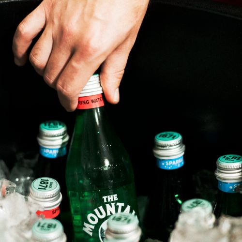 hand reaching into an ice filled cooler and grabbing a glass bottle of Mountain Valley Spring Water