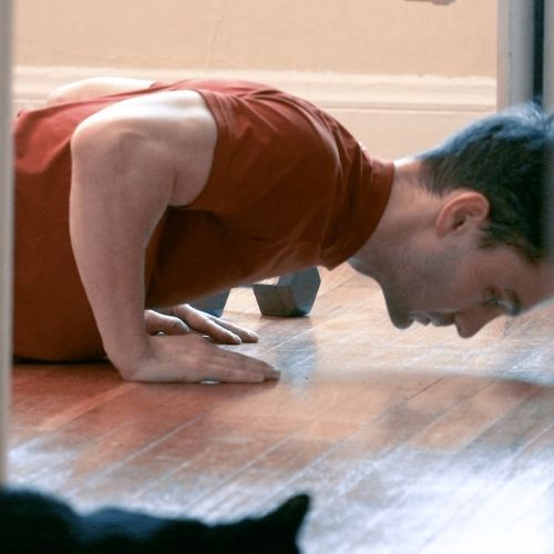 man doing push ups at home with cat watching