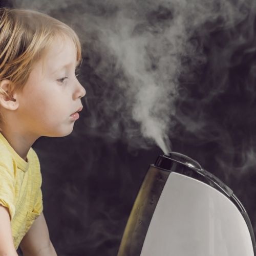 young boy breathing steam from humidifier