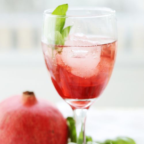glass of cranberry pomegranate spritzer next to pomegranate