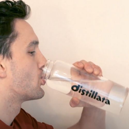 profile of man drinking water from a clear glass bottle with distillata logo