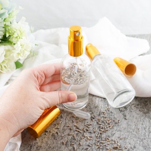 hand holding a clear glass spray bottle filled with diy lavender toner water