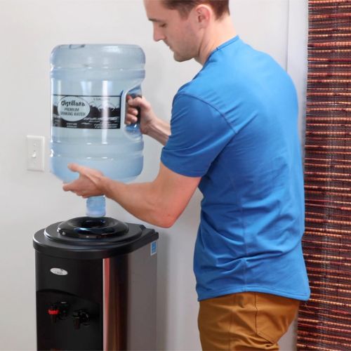 person lifting an empty Distillata 5-gallon water bottle off a water cooler