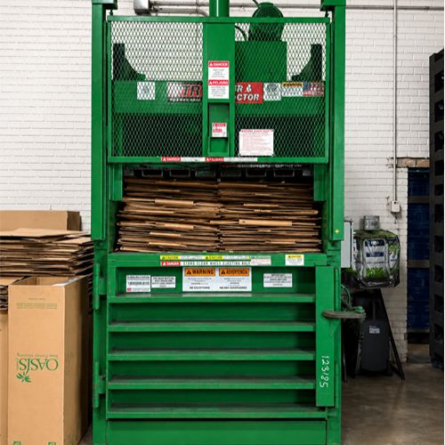 Cardboard stacked inside a green industrial baler for recycling.